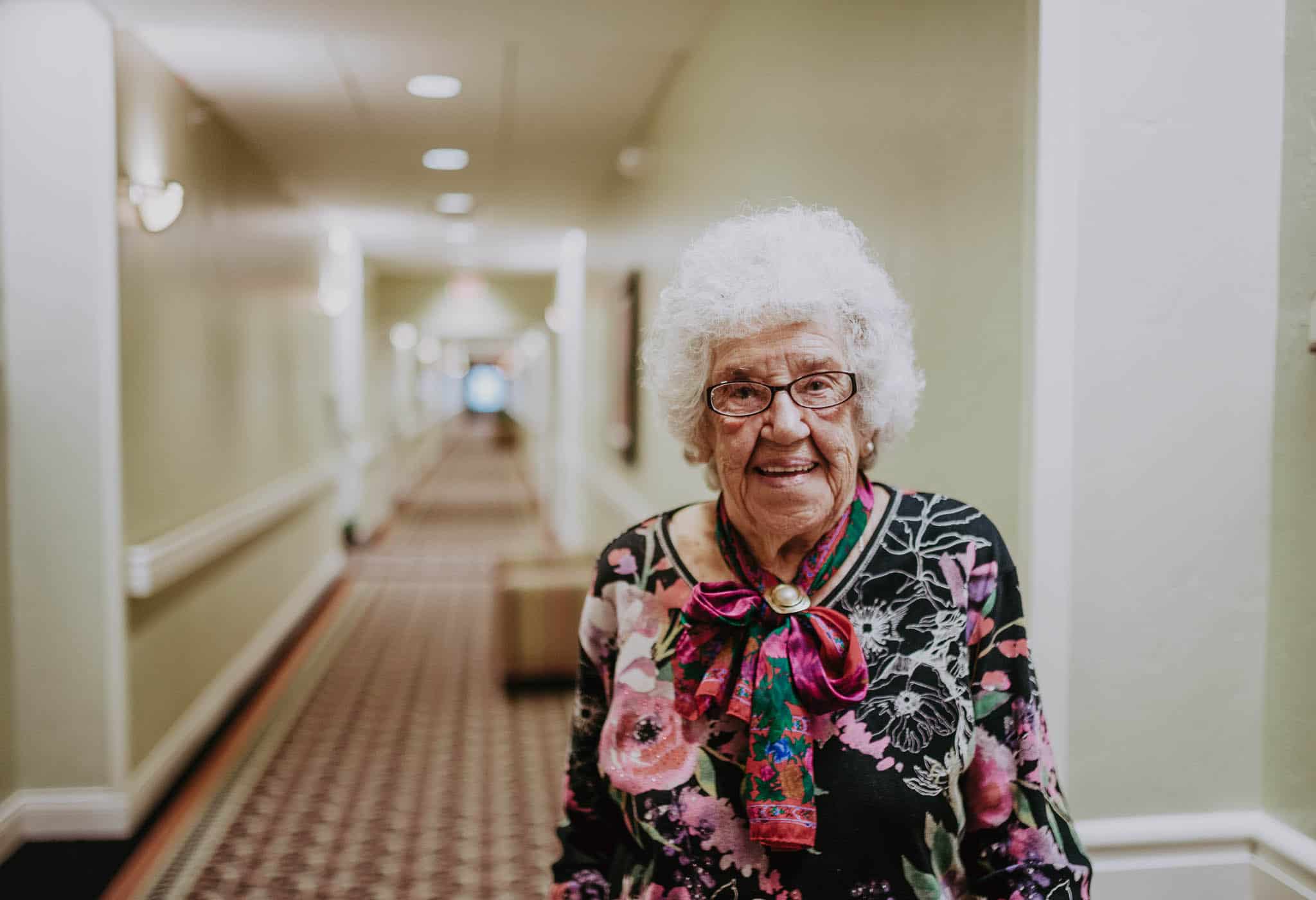 A senior woman stands in the hallway of her living community.
